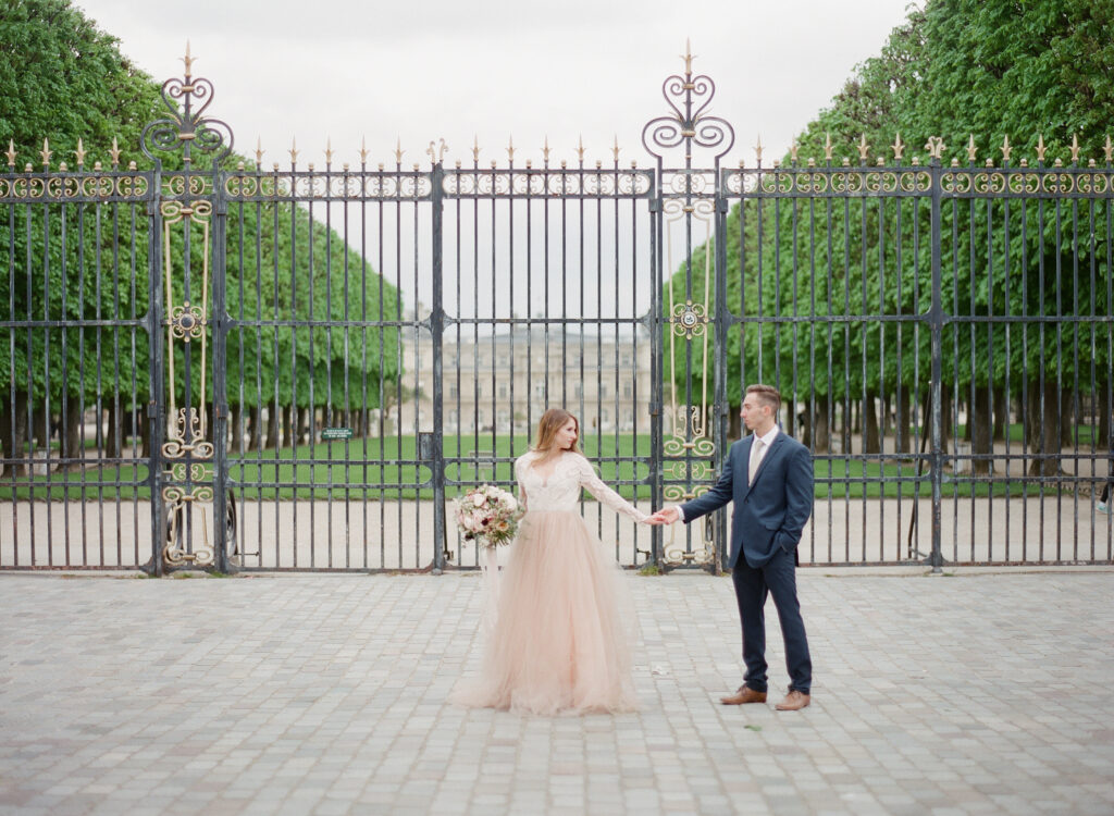 bride and groom walking in front of large black iron gates in Paris