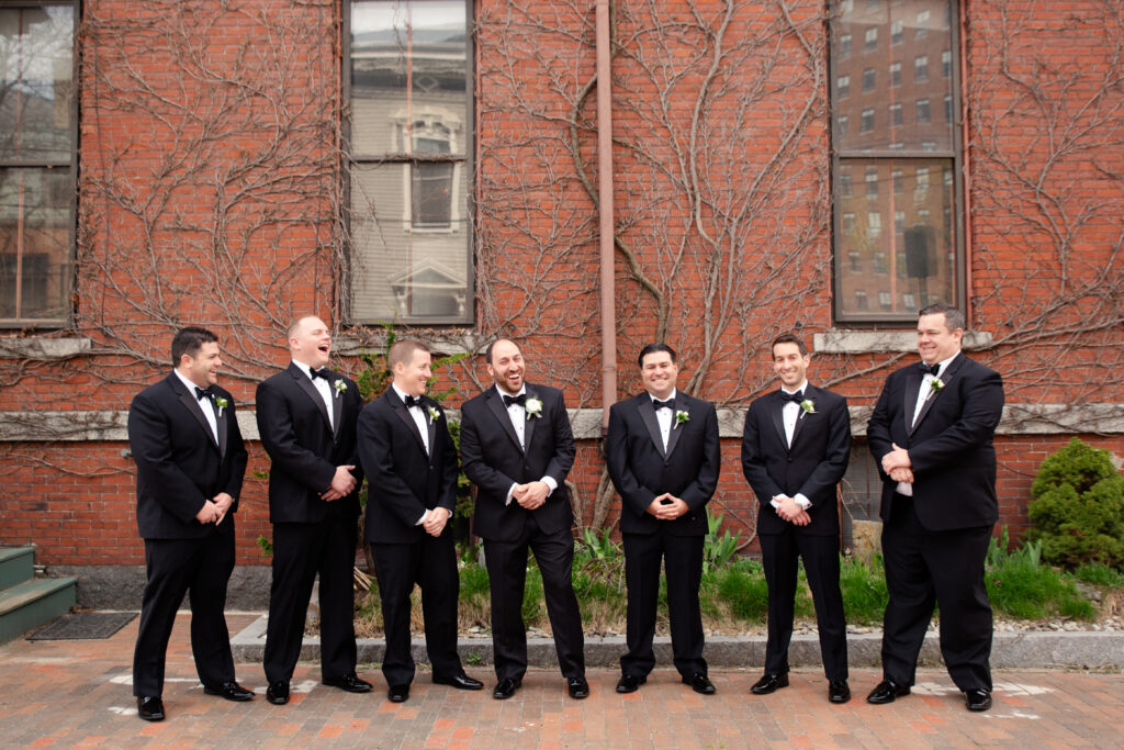 groomsmen in black tie tuxedos in front of a brick building 