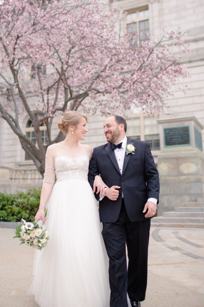 bride and groom walking in front of pink spring flowering tree