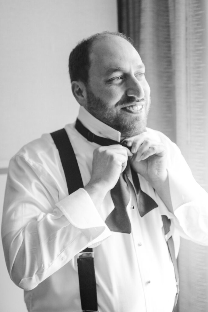 black and white photo of the groom tying his bowtie 