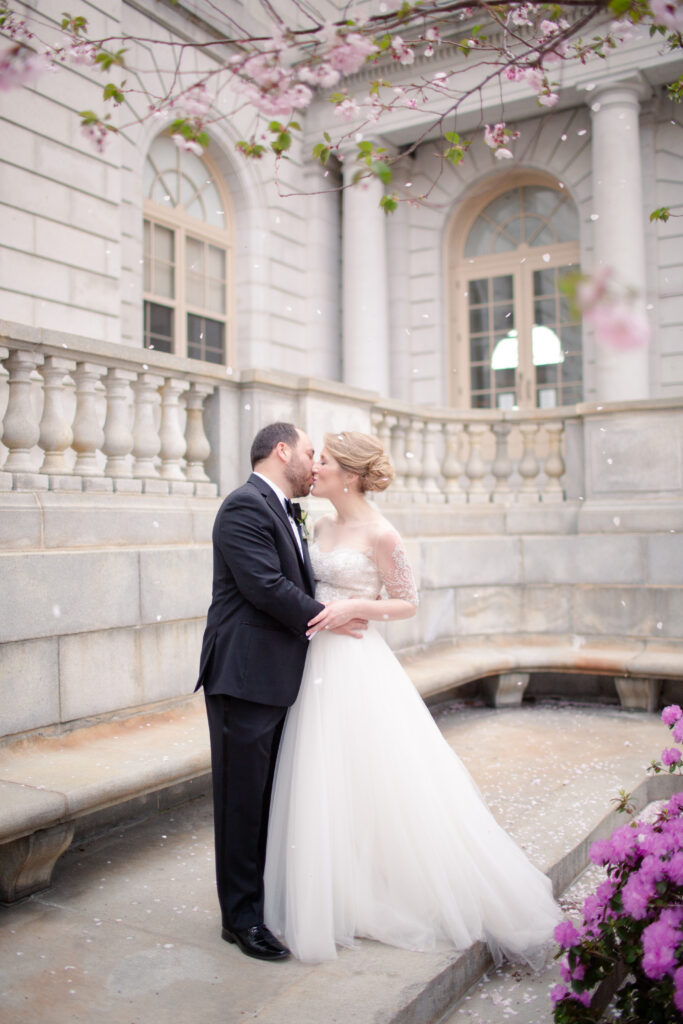 bride and groom kissing under pink flower tree losing petals 