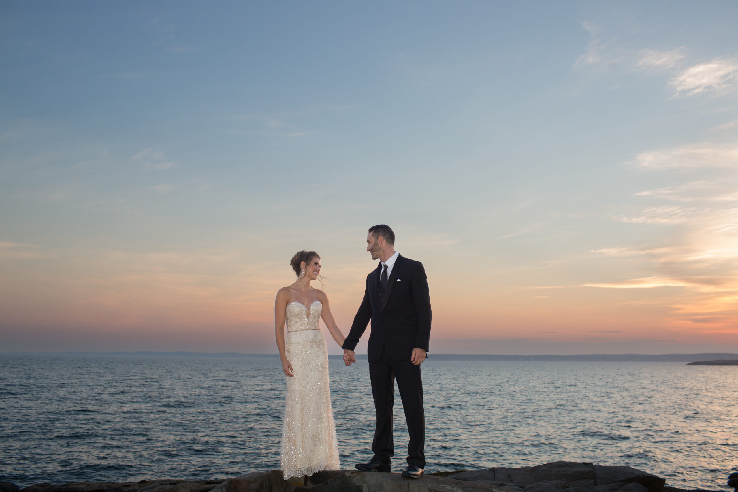 bride and groom on rocks by the ocean at sunset